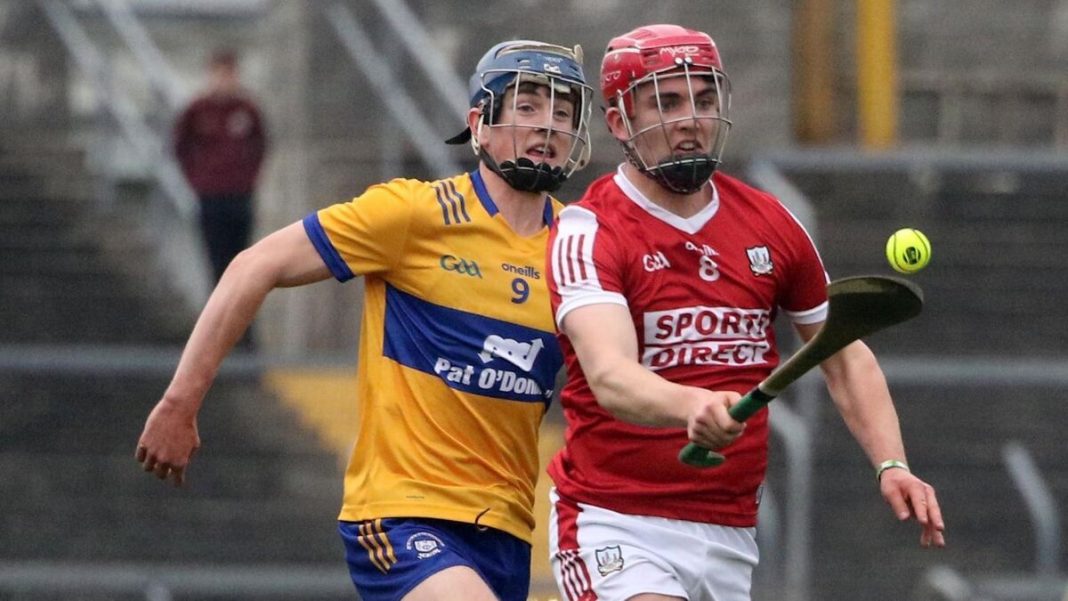 Cork hurler running with the sliotar ahead of a Clare player